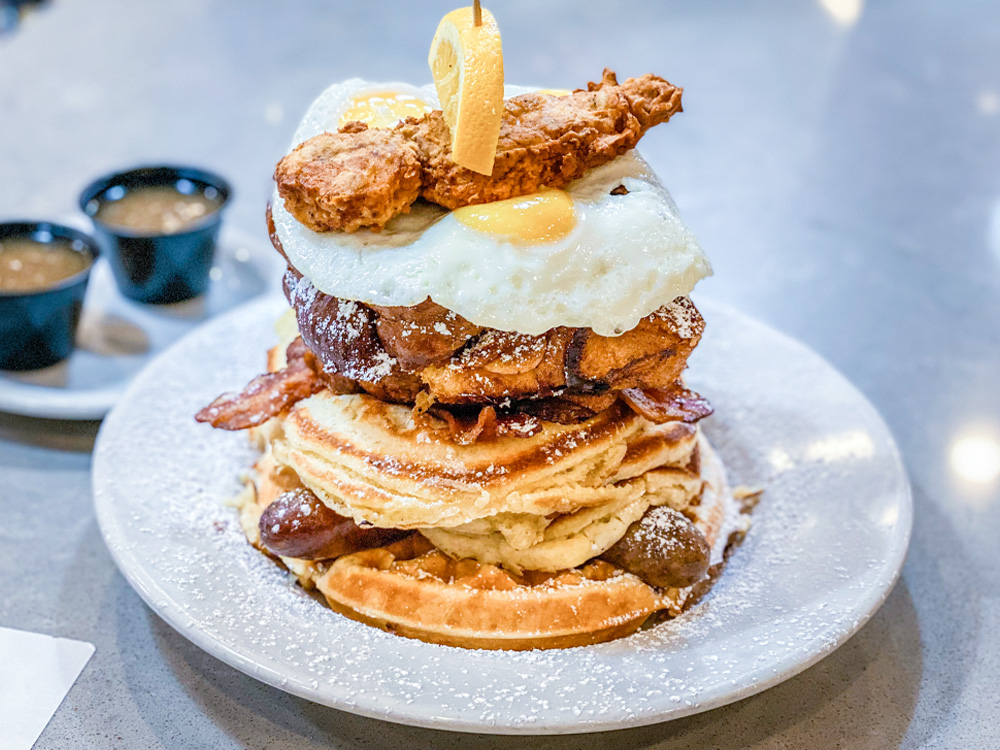 Max and Louie's Robert Stack Challenge. Waffle topped with links of sausage, three pancakes, strips of bacon, two slices of challah french toast, three eggs, a chicken tender, and orange slice.